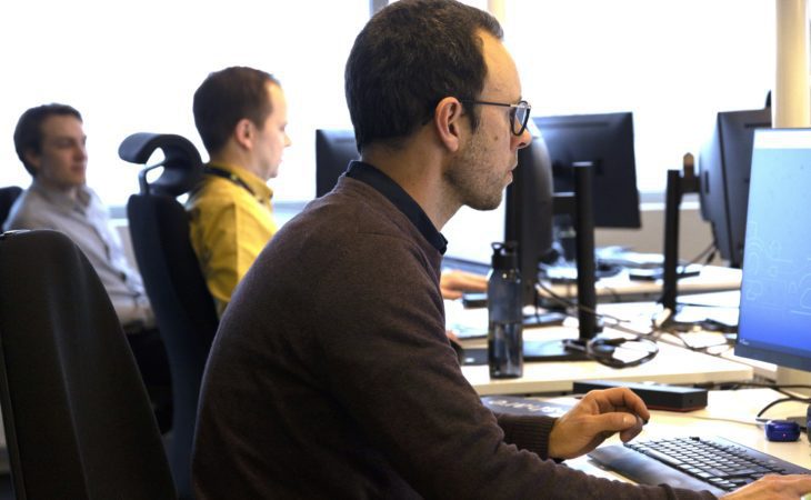 Three guys sitting next to each other working on their computers in an office environement.